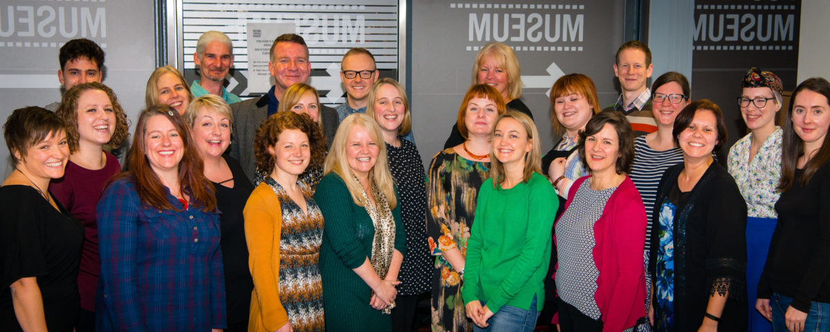 Curious Minds Team. A large group of people from a range of ages and hairstyles - predominantly women and all smiling!