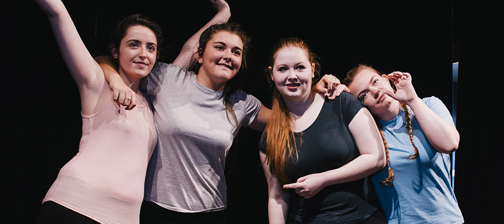 4 school girls in their own clothes holding onto one another in support.