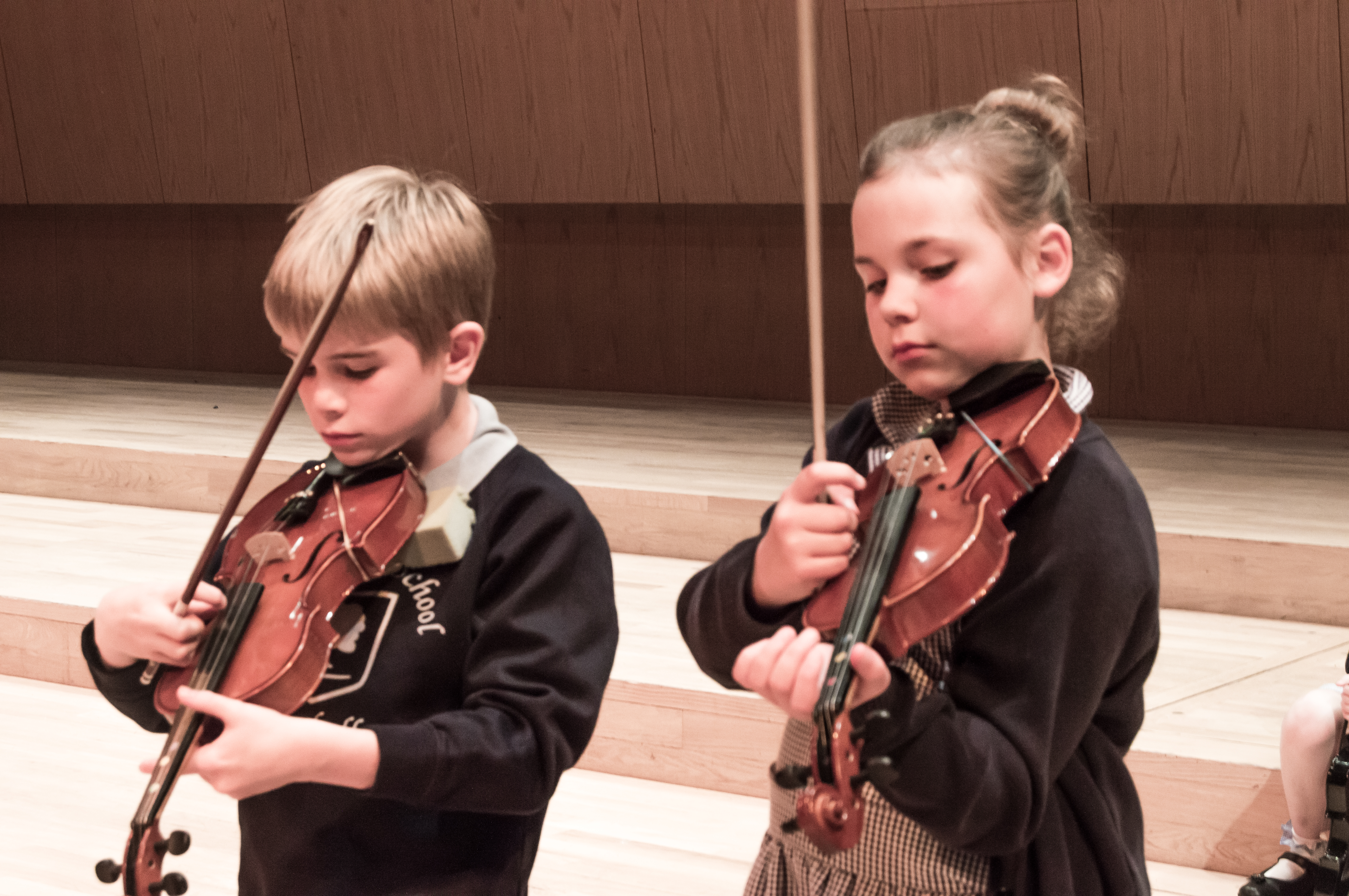 Young school boy and girl learning to play the violin with concentration.