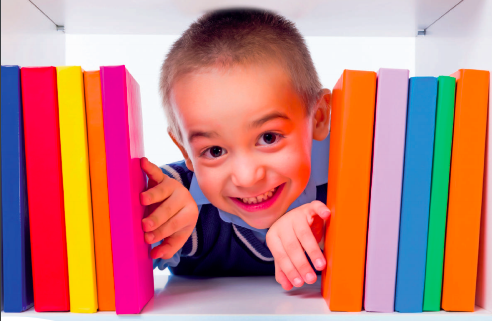 Small school child poking his through a bunch of vibrant coloured library books on a shelf.