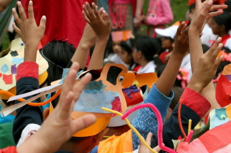 Diverse group of arms in the air, handmade dogs can be seen on the top of children's heads.