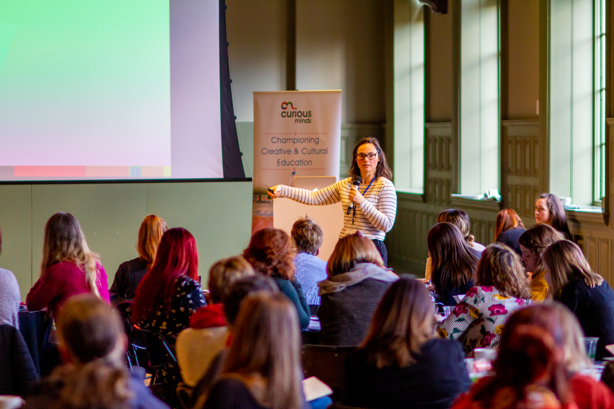 Woman stood in front of a group of people and pointing to a projector screen.