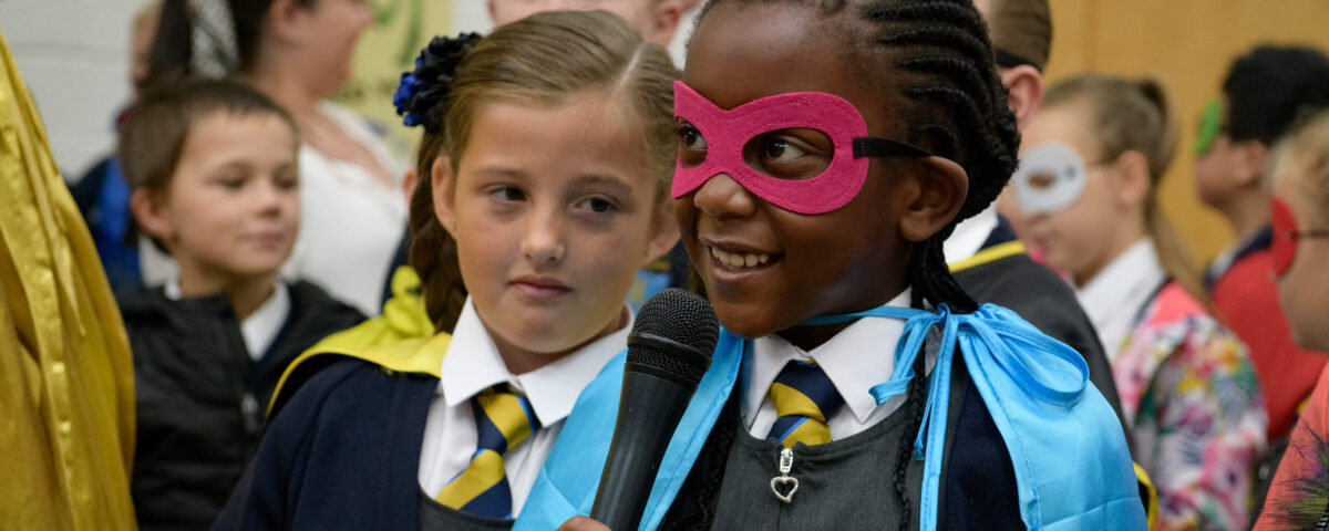 A young school pupil wearing a cape and mask speaks confidently into a microphone - From WoW's Super Heroes project.