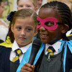 A young school pupil wearing a cape and mask speaks confidently into a microphone - From WoW's Super Heroes project.