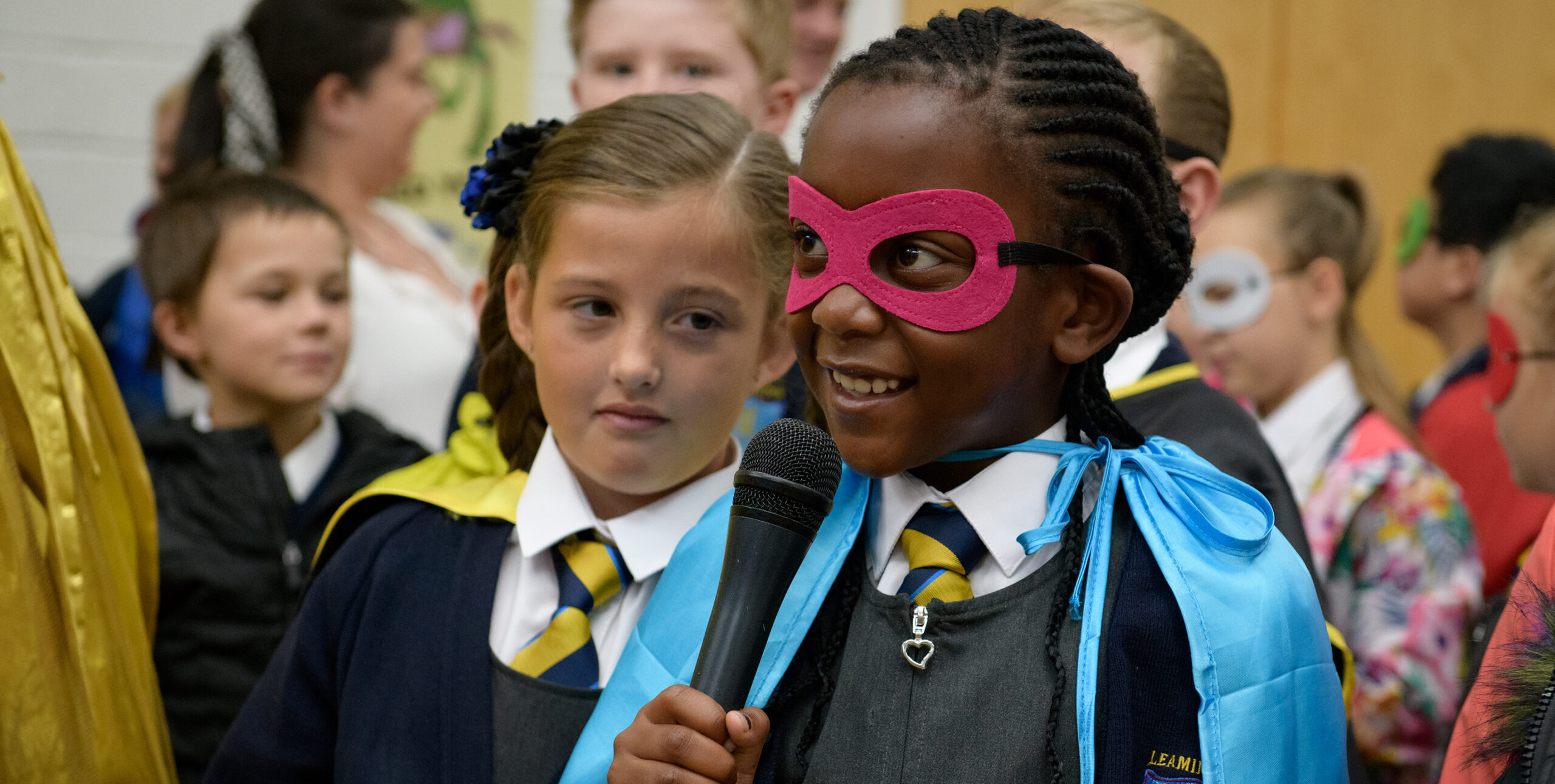 A young school pupil wearing a cape and mask speaks confidently into a microphone - From WoW's Super Heroes project.