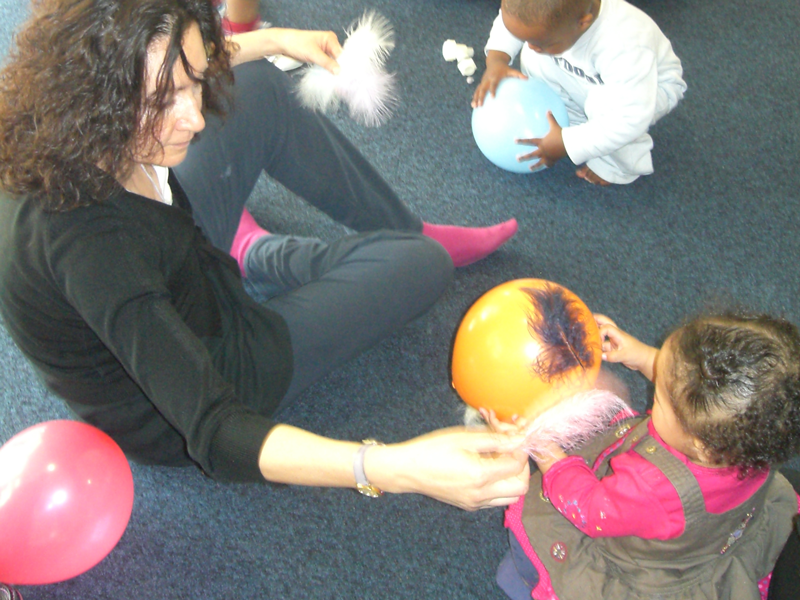 An adult is sitting on the floor with a very young child. They are playing with feathers and balloons.