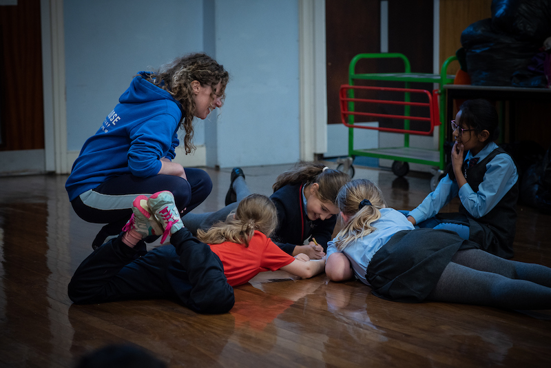 A group of chool children work on the floor with a dance practitioner