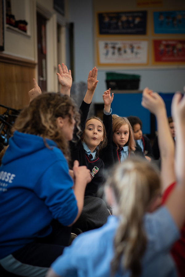 Pupils at primary school working with a dance artist. A child has her hand raised looking engaged and excited.