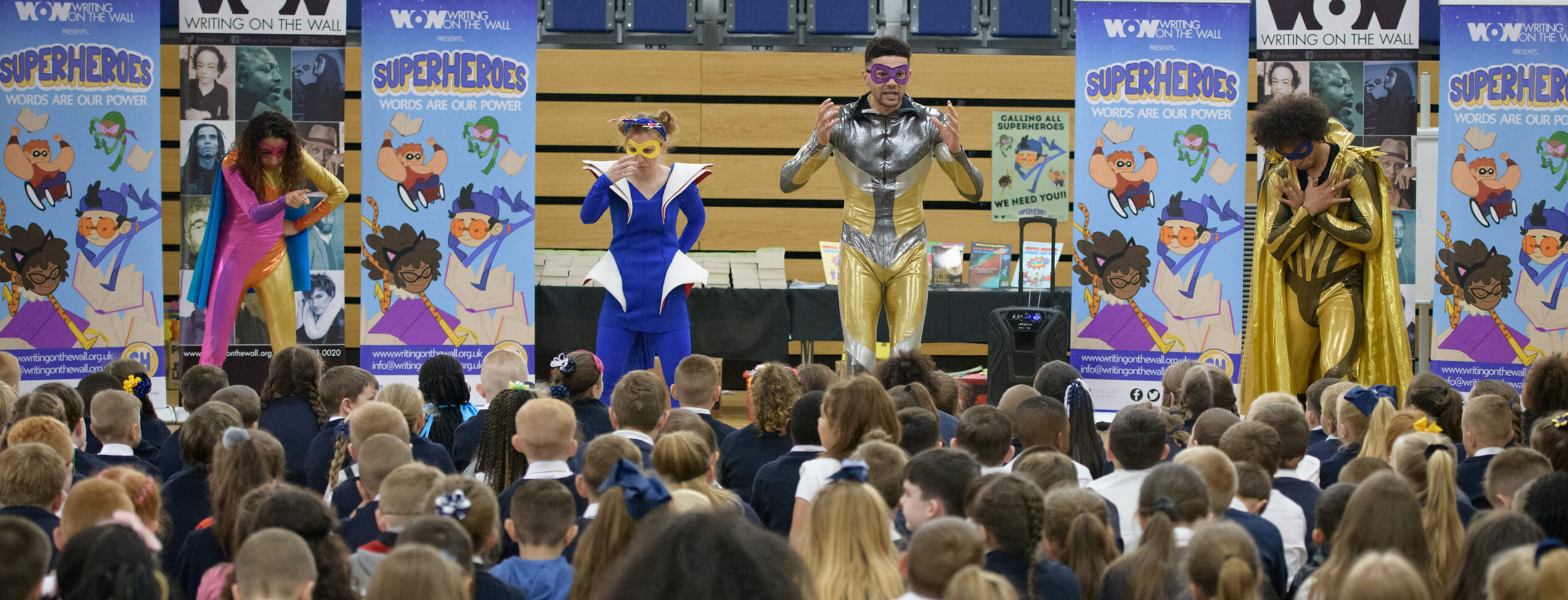 School children listen and watch attentively to four performers, dresses as superheroes, for the WoW Words are our Power project.