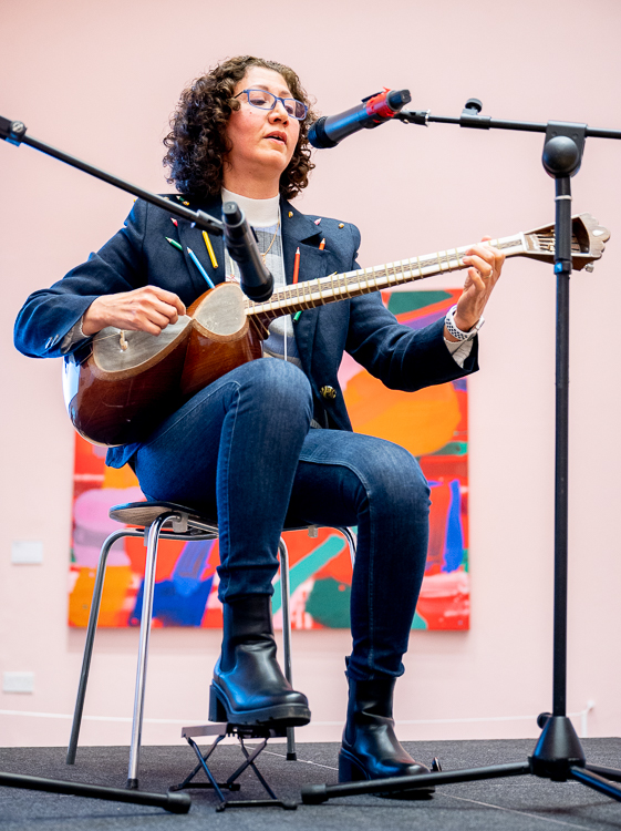Fariba performing on stage. An Iranian woman with curly hair plying a string instrument.