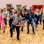 A group of people dancing led by an artist of colour.