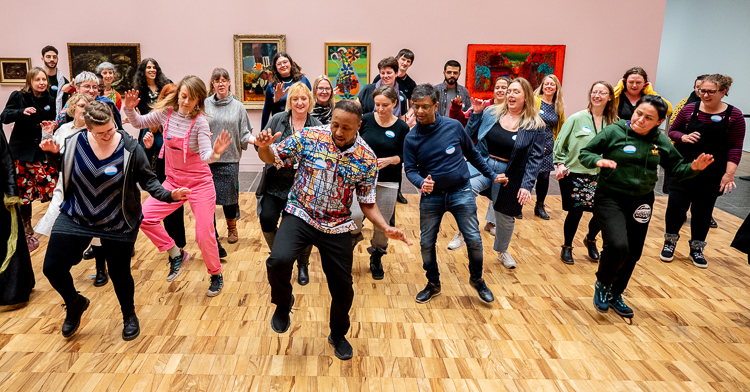 A group of people dancing led by an artist of colour.