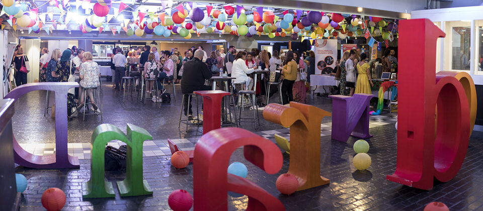 A colourful room full of people, giant coloured letters, and hanging paper lanterns.
