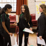 Three young people in school uniform are talking happily with each other.