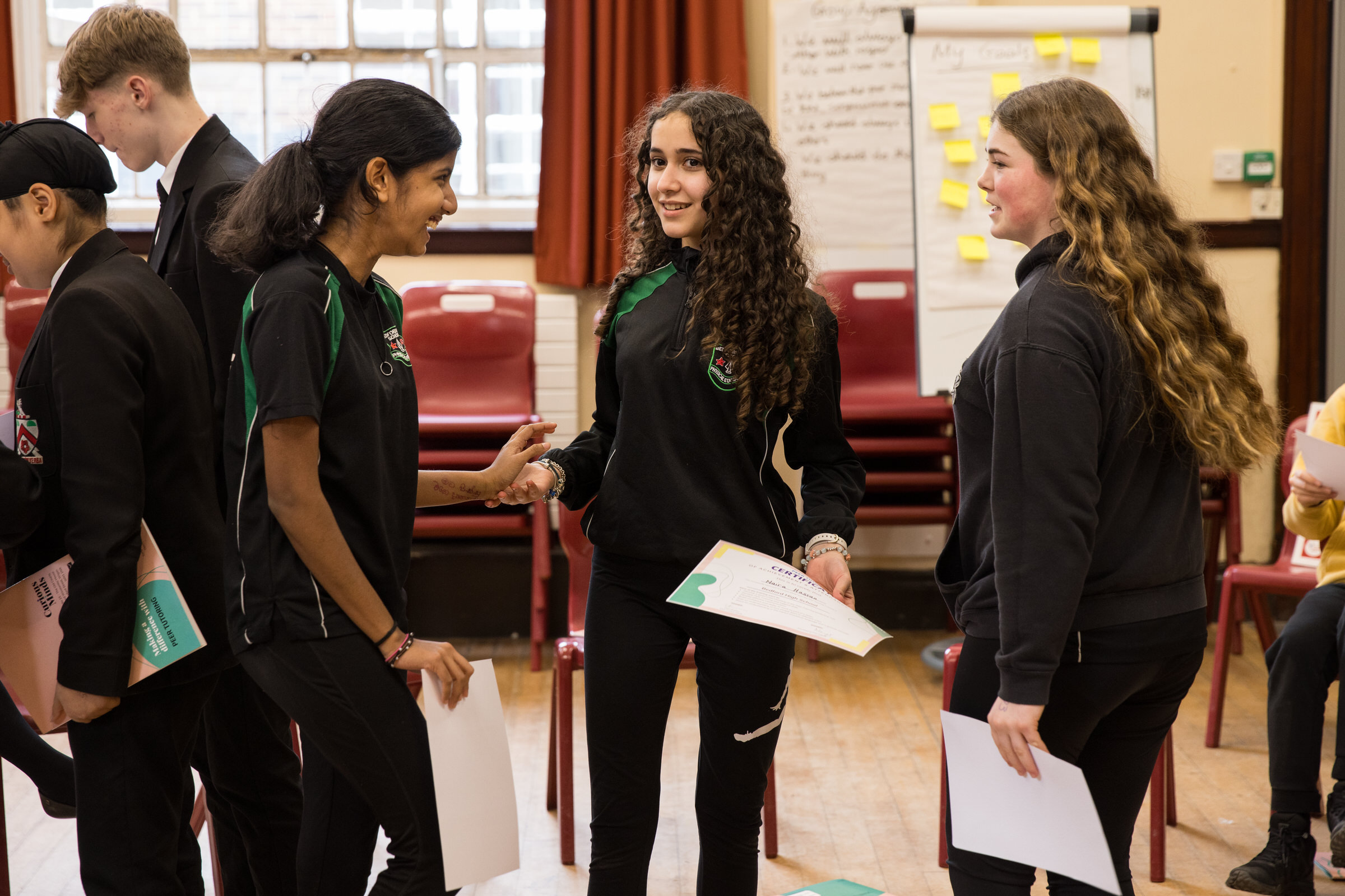 Three young people in school uniform are talking happily with each other.