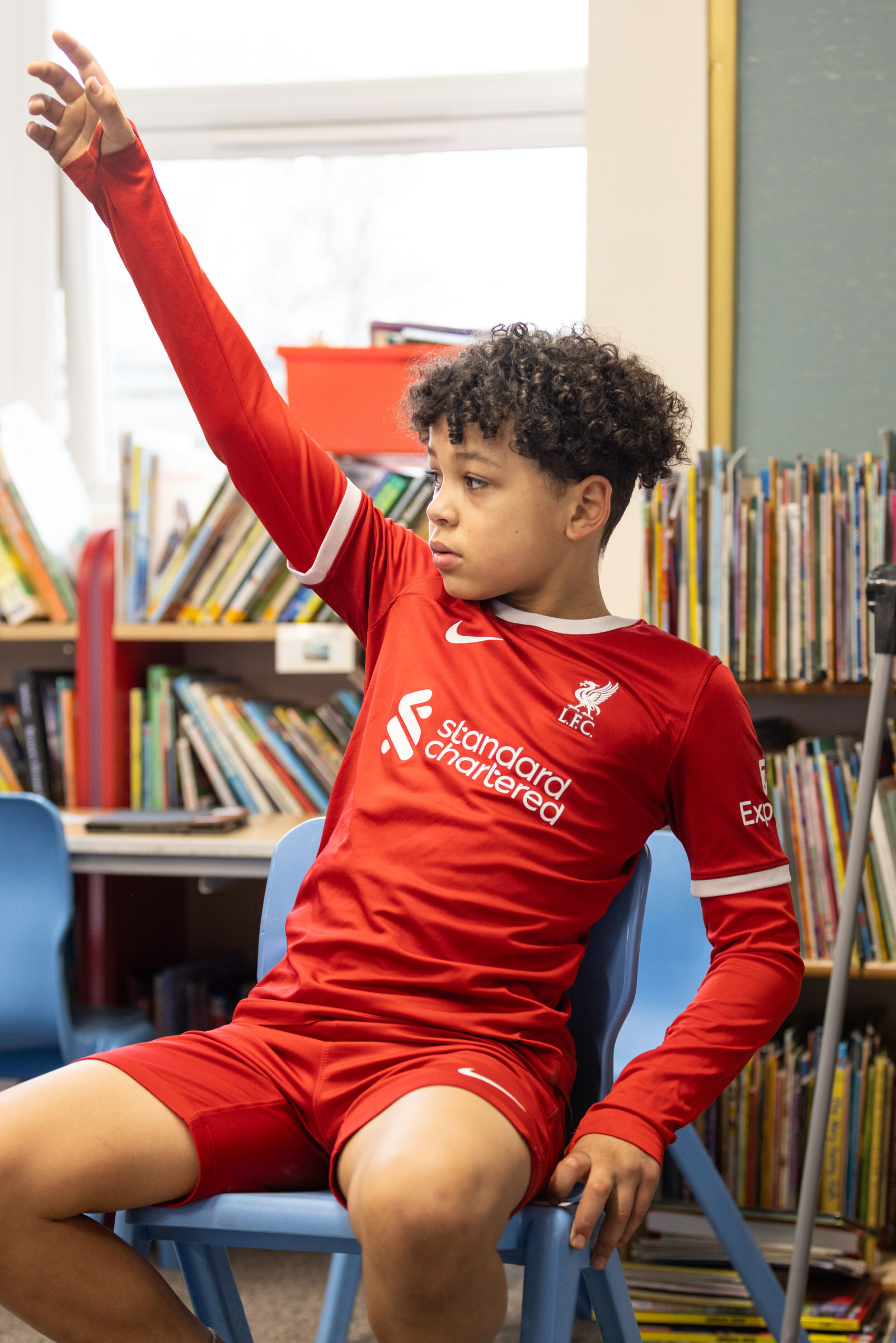 Primary school age child in a football shirt with their hand up answering a question.