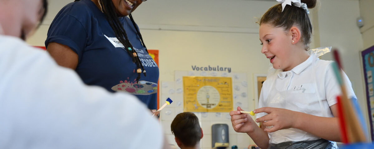 A young school pupil enjoys an interaction with her teacher whilst painting.