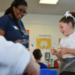 A young school pupil enjoys an interaction with her teacher whilst painting.