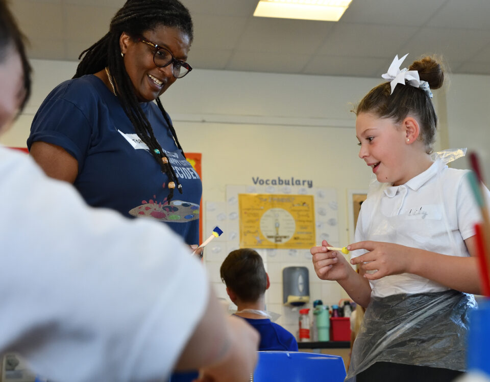 A young school pupil enjoys an interaction with her teacher whilst painting.