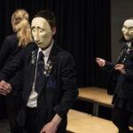 Young people in school uniform are doing a drama workshop. Two of them are using the comedy and tragedy muses masks.