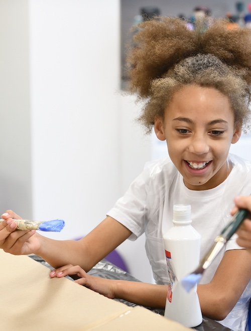 A school pupil prepares to paint in an art class. She is smiling and having fun.