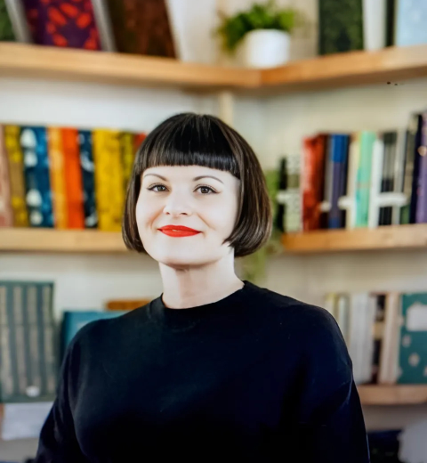 A woman with dark hair smiling with a bookcase behind them.