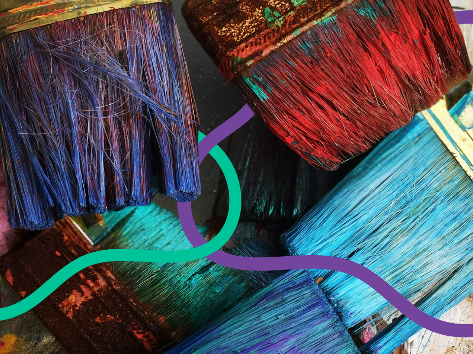 A close-up of some very colourful paint brushes with dried and wet paint still on the bristles.