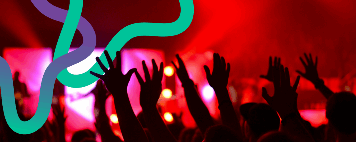 Hands in the air at a concert. Red lighting dominates as colourful squiggly lines interweave above them.