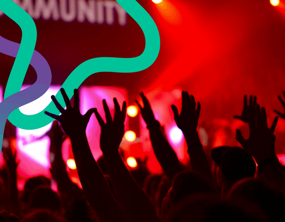 Hands in the air at a concert. Red lighting dominates as colourful squiggly lines interweave above them.