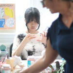 A girl with dark hair sat in a pottery class taking a photo of her work.