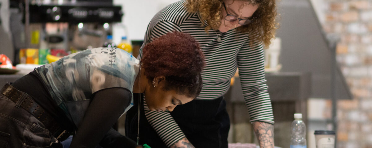 Two young people are working together, stood at a table writing on paper with a felt tip