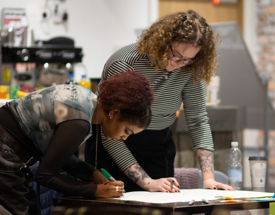 Two young people are working together, stood at a table writing on paper with a felt tip